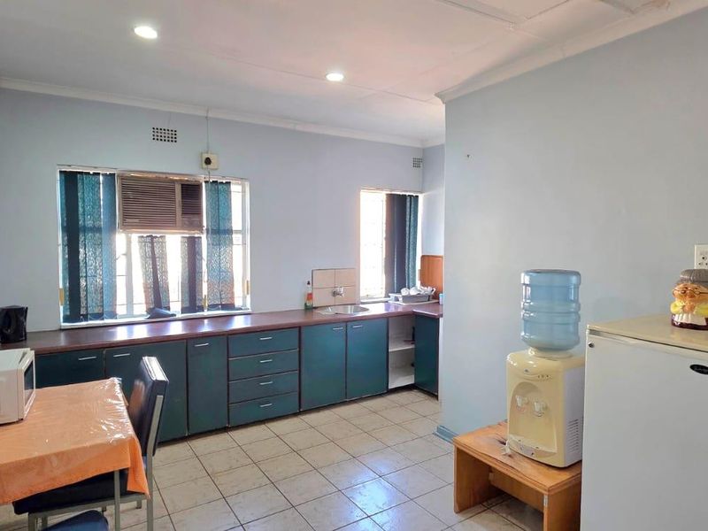 A functional office kitchen area featuring built-in cabinetry, laminate countertops, a stainless steel sink, and tiled flooring with recessed lighting.
