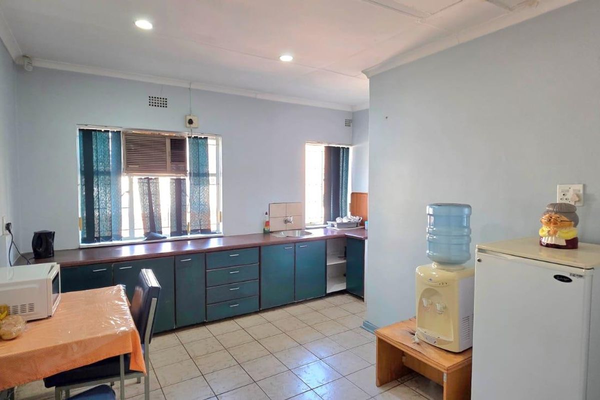 A functional office kitchen area featuring built-in cabinetry, laminate countertops, a stainless steel sink, and tiled flooring with recessed lighting.