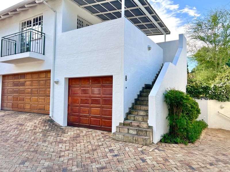 Front exterior view of the apartment featuring a brick paved driveway, wooden garage doors, and an external staircase leading to an upper balcony.