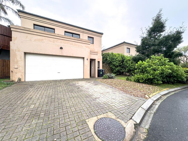 Front elevation of a townhouse featuring a double garage, paved driveway, and established garden area with visible exterior paint wear.
