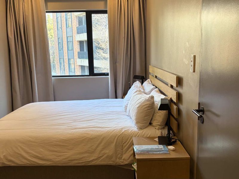 A compact bedroom featuring neutral wall tones, a large window with curtains, and standard internal door access.