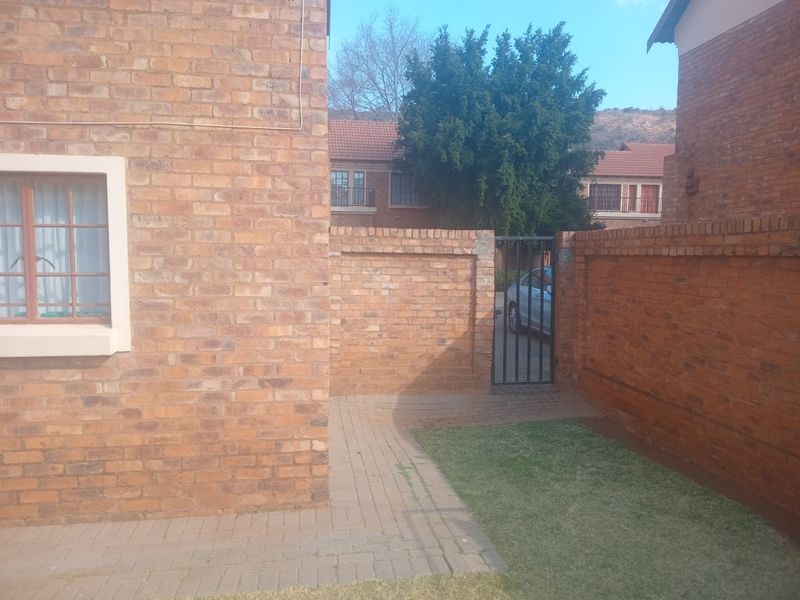 A private rear courtyard area featuring face brick walls, a paved walkway, and a small lawn section with a metal security gate.