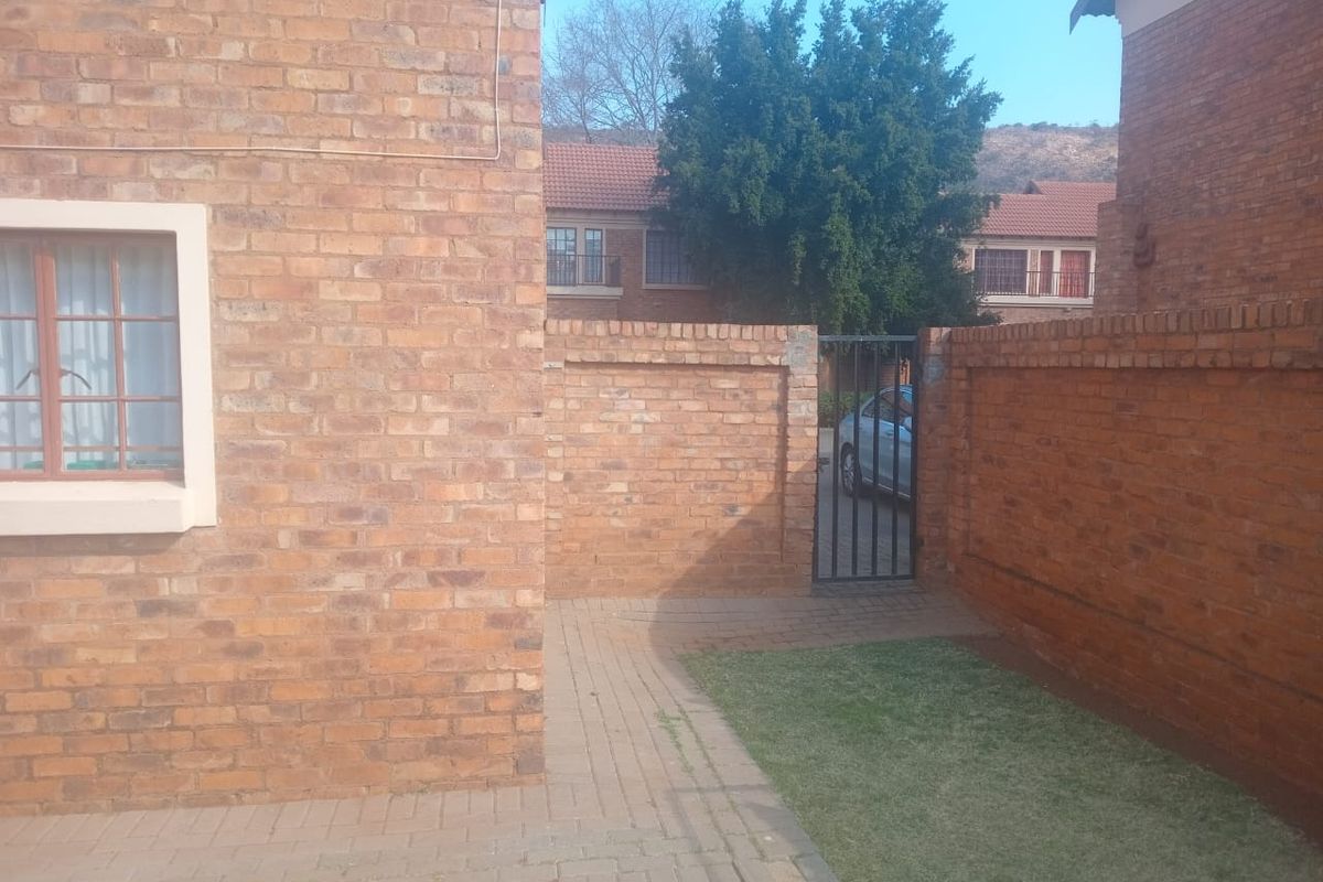 A private rear courtyard area featuring face brick walls, a paved walkway, and a small lawn section with a metal security gate.