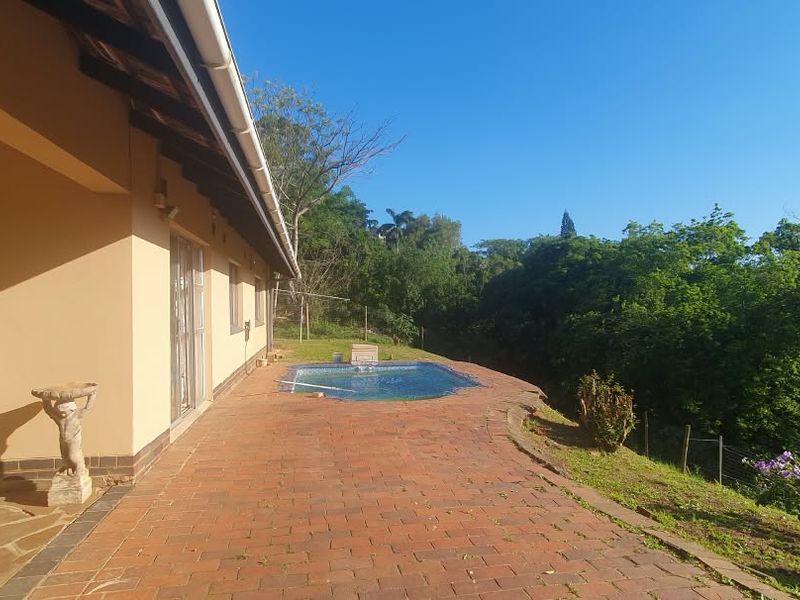 Outdoor pool area featuring a brick-paved patio, covered veranda, and scenic views of the surrounding landscape.