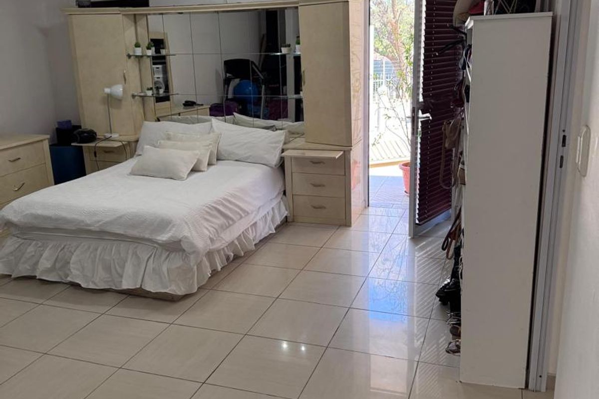 Spacious bedroom featuring tiled flooring, a built-in mirrored headboard unit, and a wall-mounted air conditioning unit with direct access to an outdoor area.