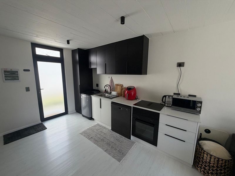 Modern kitchen featuring sleek black and white cabinetry, integrated oven, hob, and a functional sink area with direct access to an exterior door.