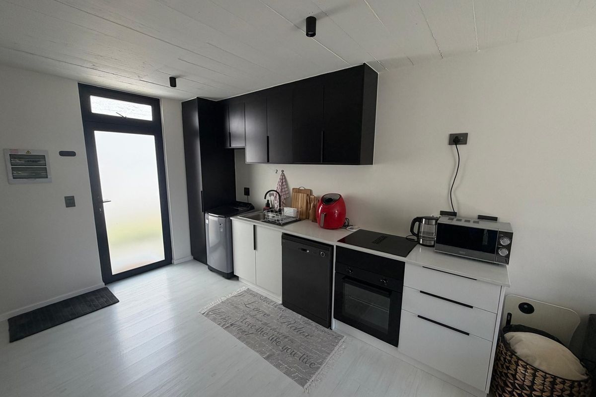 Modern kitchen featuring sleek black and white cabinetry, integrated oven, hob, and a functional sink area with direct access to an exterior door.