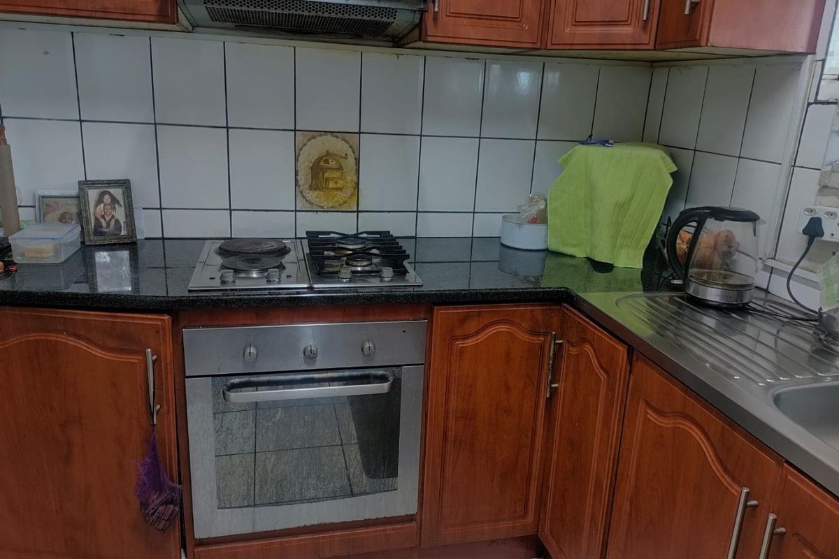A functional kitchen featuring wooden cabinetry, granite countertops, a built-in oven with a dual gas and electric hob, and a stainless steel sink.