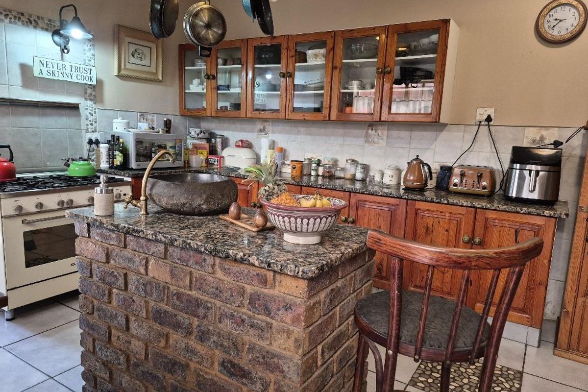 A rustic-style kitchen featuring a brick-based island with a stone basin, granite countertops, and traditional wooden cabinetry.
