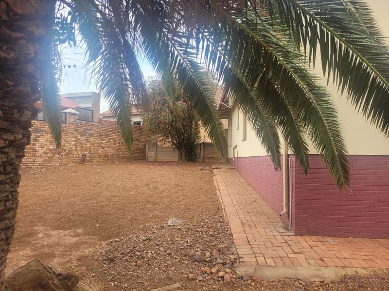 A view of the rear garden area featuring a paved walkway along the side of the house and a brick boundary wall.