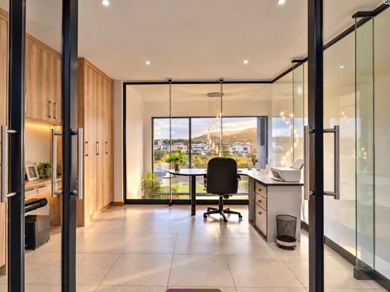 Modern home office featuring sleek built-in cabinetry, glass partition walls, and large windows offering scenic views, creating a bright and professional workspace.