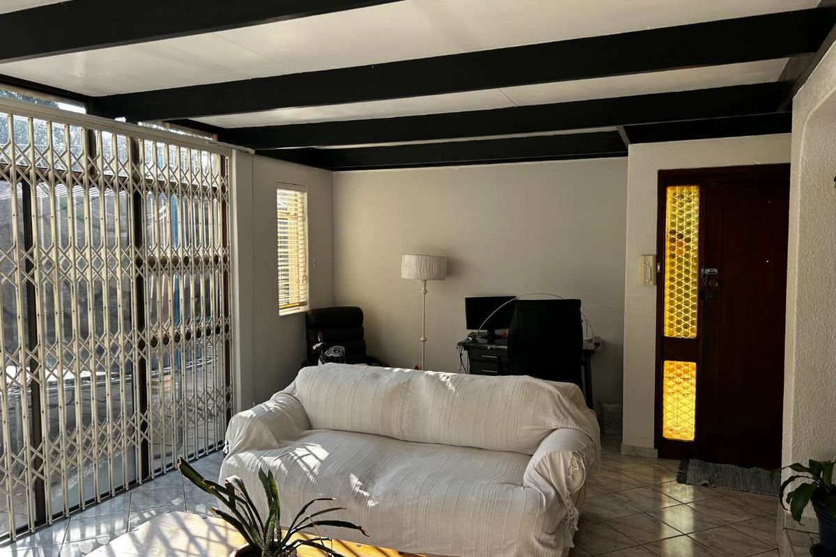 A living area featuring exposed ceiling beams, tiled flooring, and a security gate leading to the exterior.