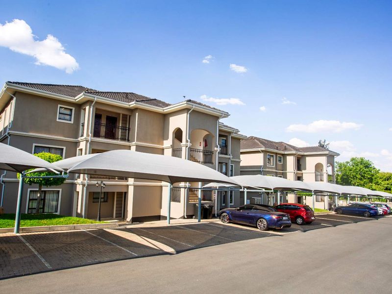 Exterior view of a modern apartment complex featuring paved parking bays with shade cloth carports and well-maintained building facades.