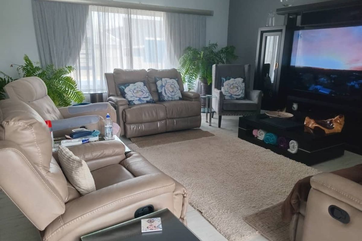 A comfortable living room featuring light-toned laminate flooring and large windows with sheer curtains, providing a bright and inviting space.