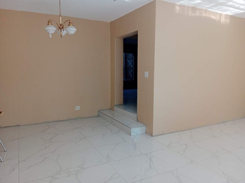 An empty living area featuring modern marble-look floor tiles, a raised step transition, and a classic chandelier, ready for personalization.