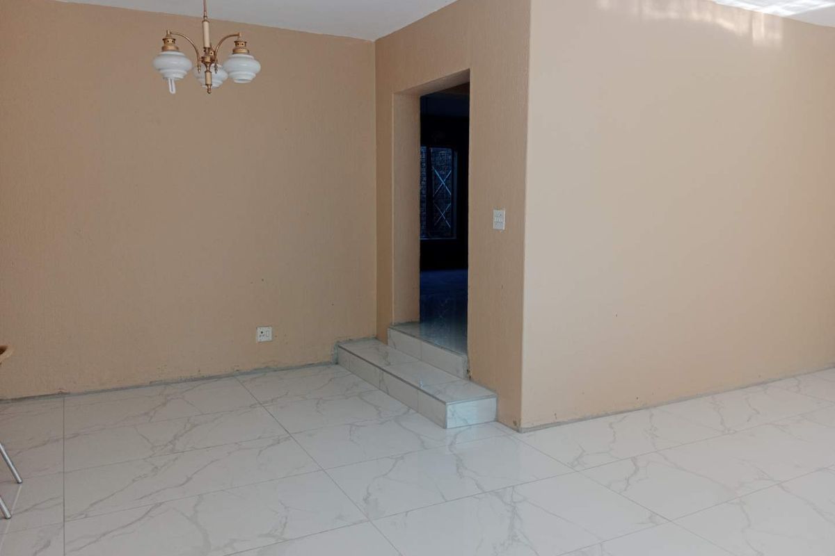 An empty living area featuring modern marble-look floor tiles, a raised step transition, and a classic chandelier, ready for personalization.