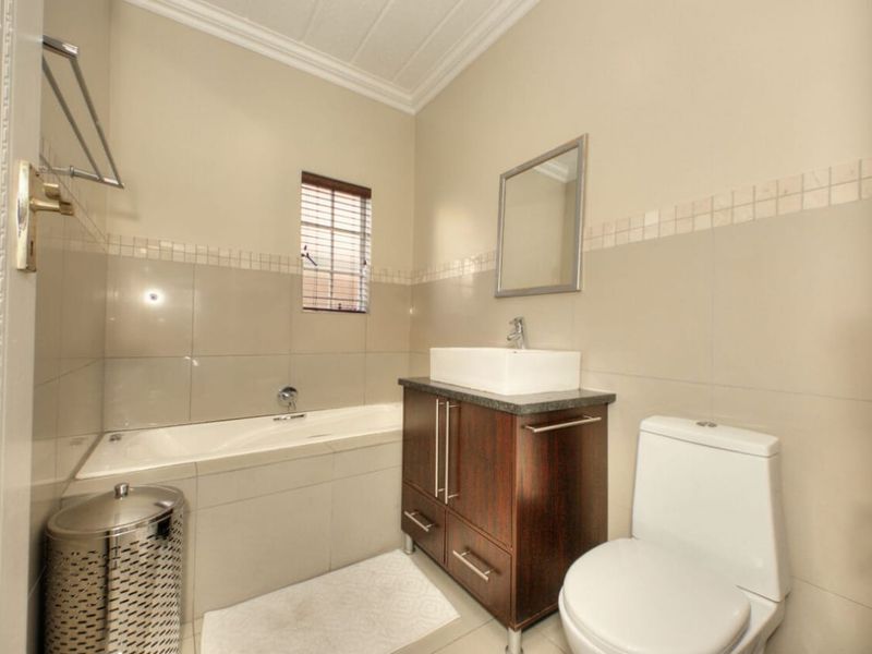 A well-maintained bathroom featuring a built-in bathtub, a modern vessel sink with a dark wood vanity cabinet, and neutral wall tiling.