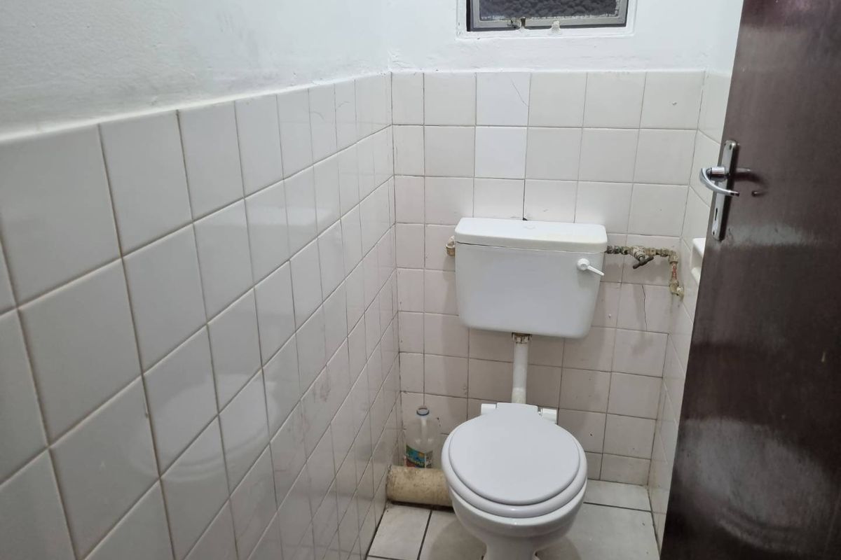 A compact bathroom featuring white wall tiles, a standard toilet, and a small high-level window.