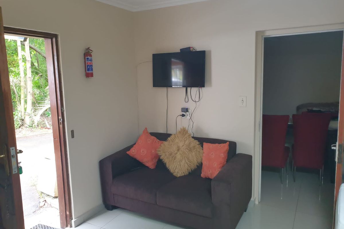 A compact living area featuring tiled flooring and direct access to the exterior, with a wall-mounted television and fire safety equipment.
