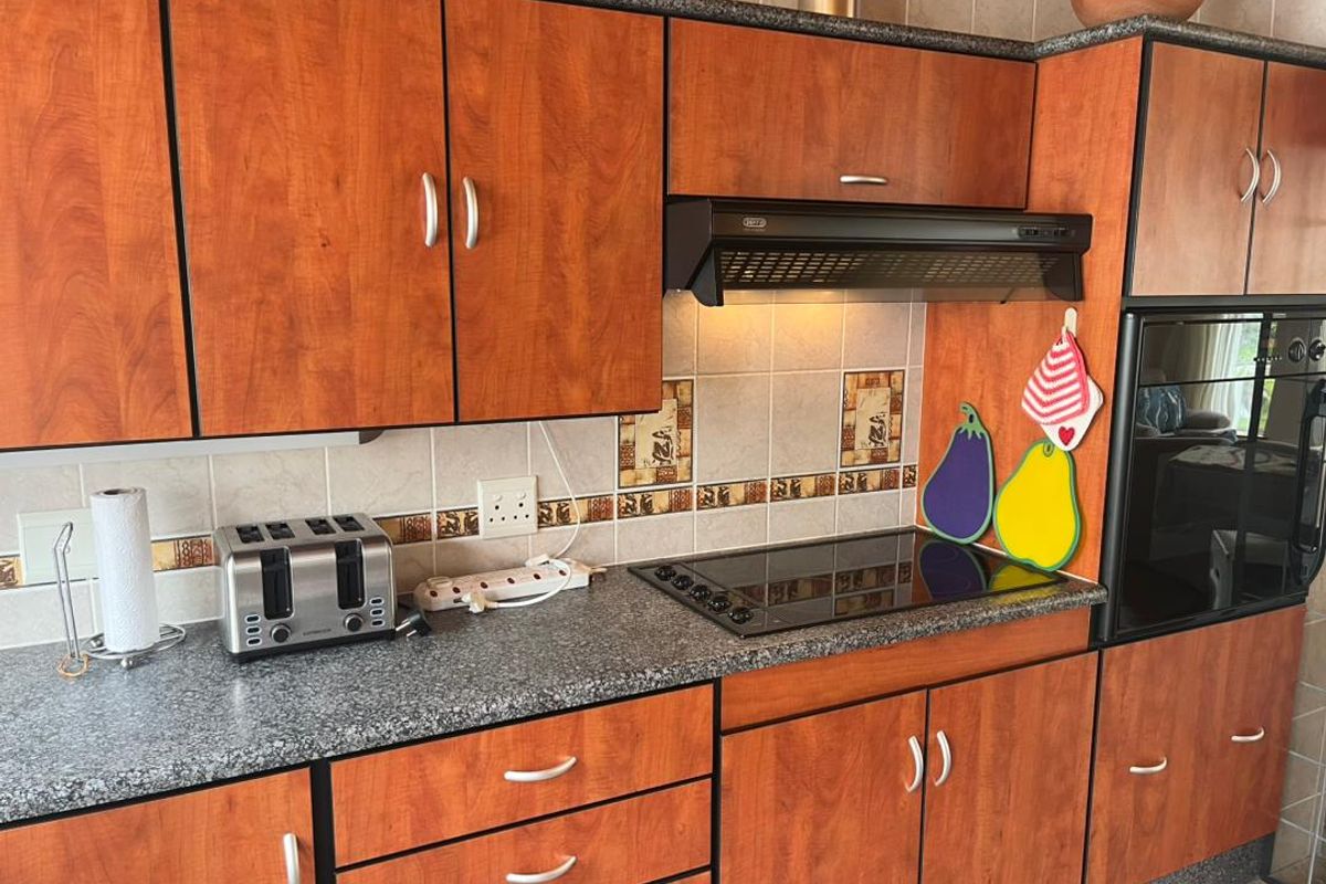 A functional kitchen featuring wood-look cabinetry, granite-style countertops, a built-in oven, and a black glass cooktop with an extractor fan.