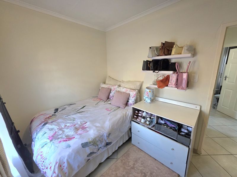 A compact bedroom featuring tiled flooring and wall-mounted shelving, providing a functional space with neutral wall finishes.