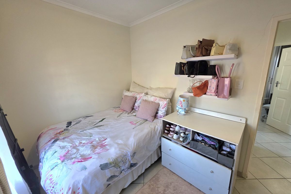 A compact bedroom featuring tiled flooring and wall-mounted shelving, providing a functional space with neutral wall finishes.
