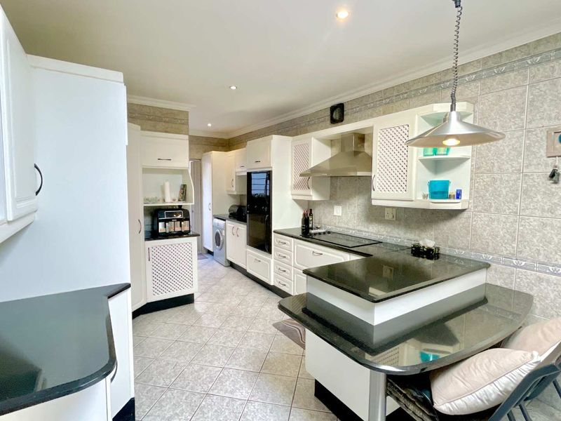 A functional kitchen featuring white cabinetry, black granite countertops, tiled finishes, built-in oven, hob, and extractor fan with integrated breakfast nook.