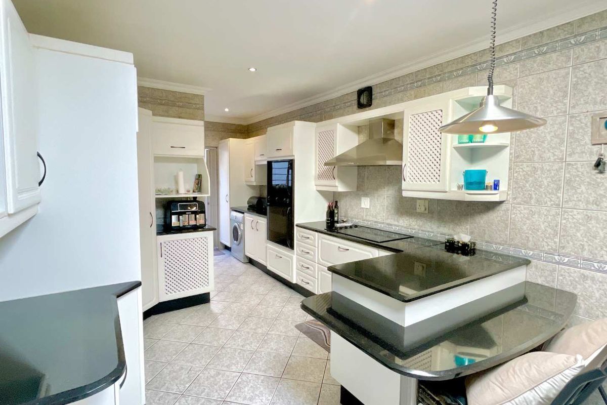 A functional kitchen featuring white cabinetry, black granite countertops, tiled finishes, built-in oven, hob, and extractor fan with integrated breakfast nook.
