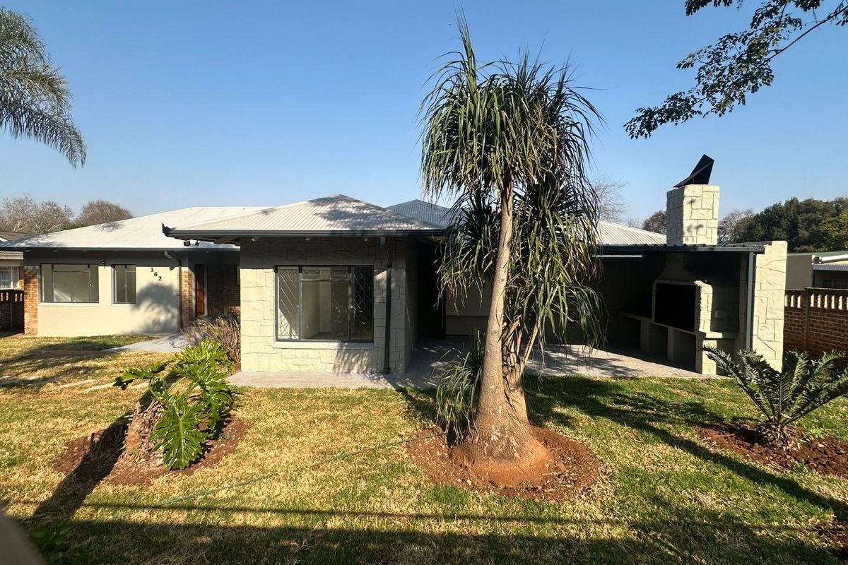 Rear view of the property featuring a paved patio area with a built-in braai, stone cladding accents, and a well-maintained garden.
