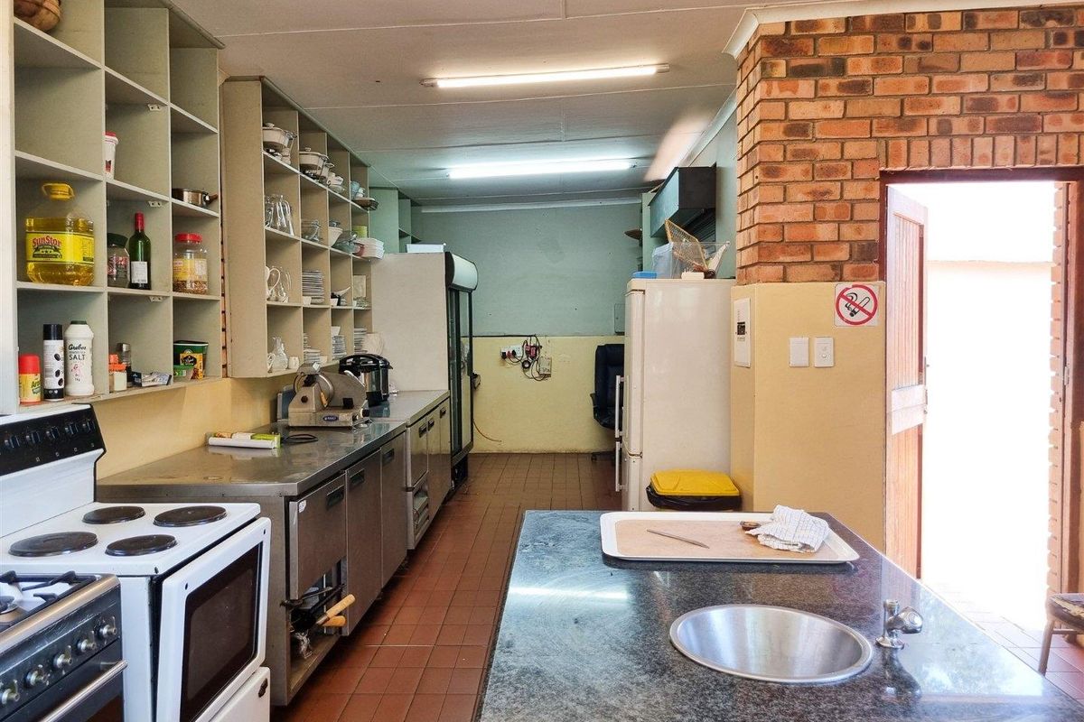 Commercial kitchen area featuring stainless steel countertops, built-in shelving, a central prep island with sink, and direct access to an outdoor area.