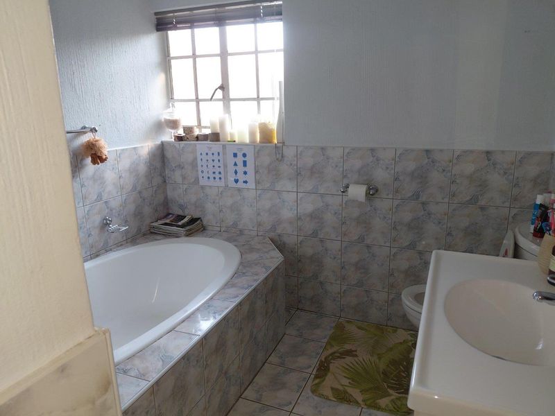 A functional bathroom featuring a built-in bathtub, tiled walls and flooring, a pedestal washbasin, and a toilet under a window.