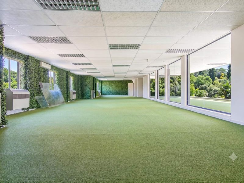 Spacious open-plan office area featuring artificial grass flooring, vertical garden walls, and large floor-to-ceiling windows providing ample natural light and garden views.