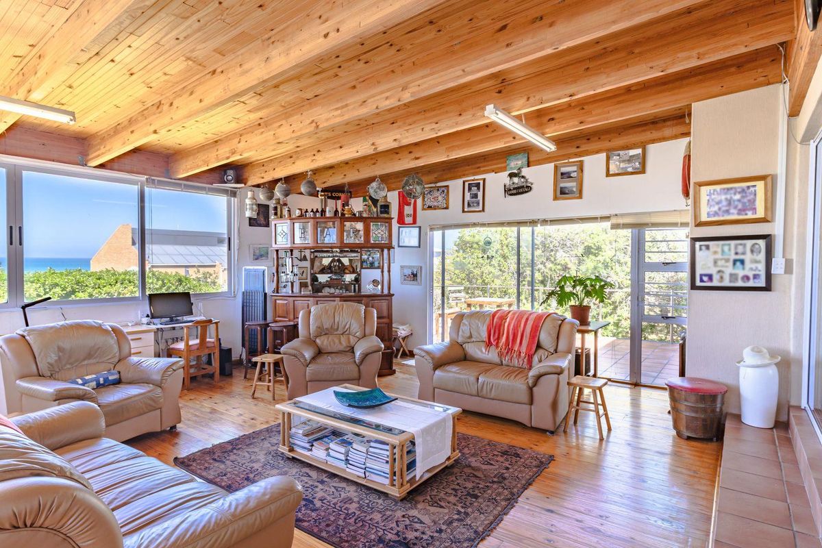 Spacious living room featuring exposed timber beam ceilings, warm timber flooring, and large windows offering natural light and scenic views.