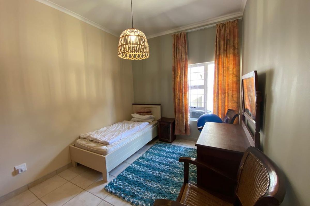 A bedroom featuring tiled flooring, a window with curtains, and a central pendant light fixture.