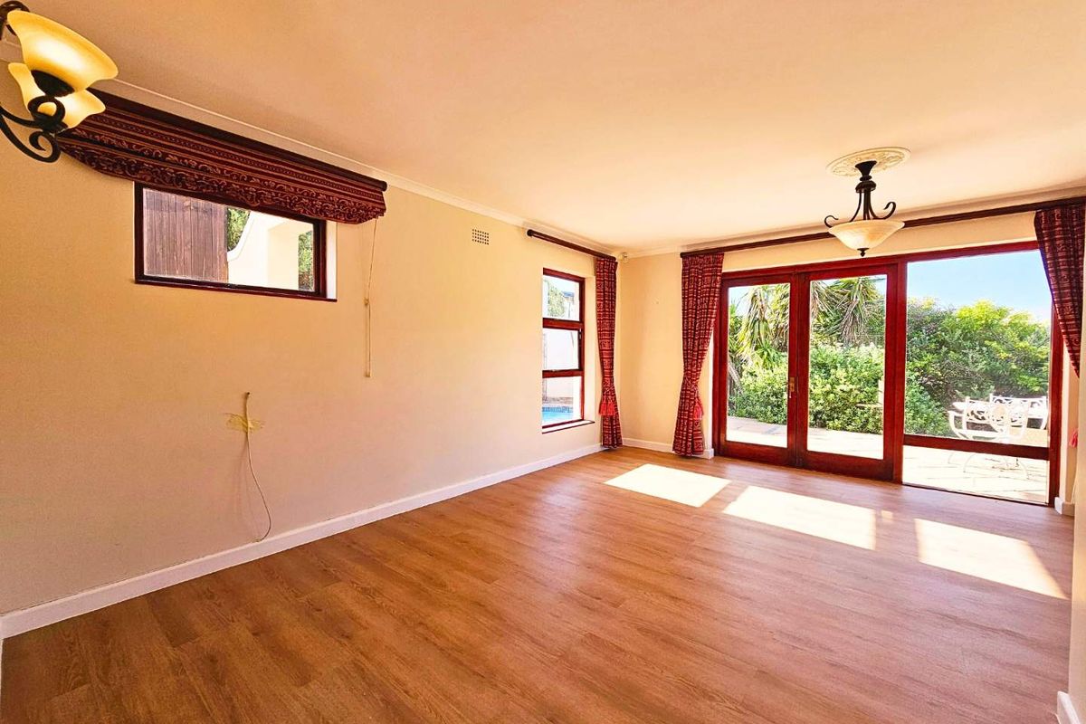 Spacious living room featuring wood-look flooring, large timber-framed glass doors opening to the patio, and classic light fixtures.