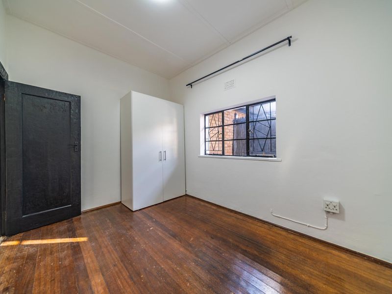 A vacant bedroom featuring original timber flooring, a window with security bars, and a neutral wall finish, offering a blank canvas for renovation.