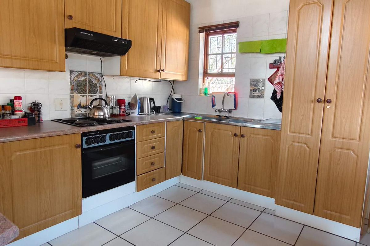 A functional kitchen featuring wood-look cabinetry, a built-in oven with hob, extractor fan, and tiled finishes throughout.