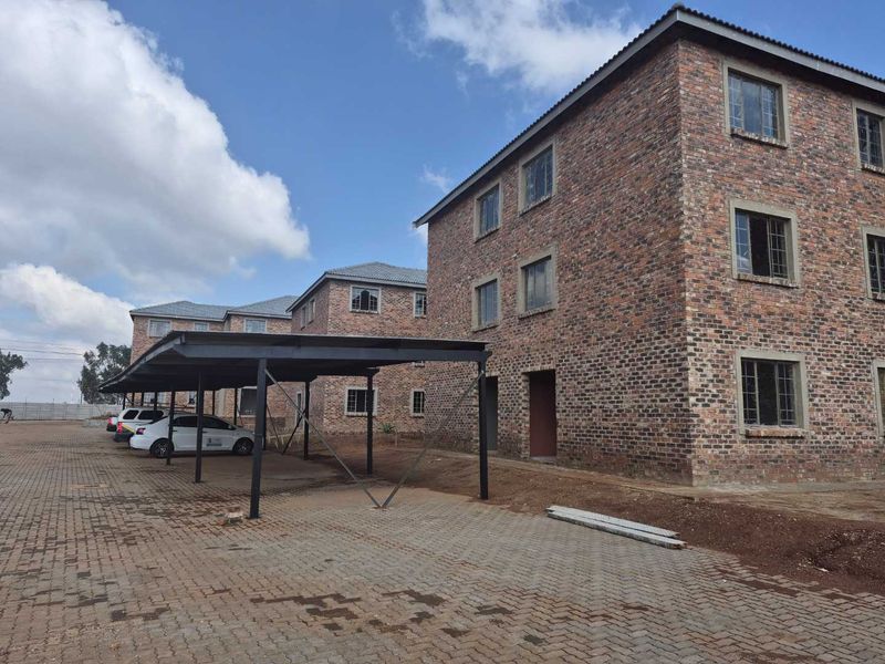 Exterior view of a multi-story apartment complex featuring face brick construction, tiled roofing, and dedicated steel carport parking bays.