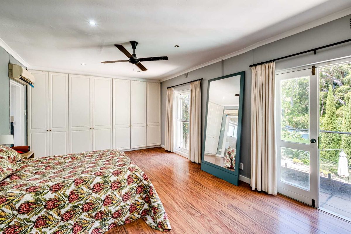 Spacious bedroom featuring extensive built-in cabinetry, timber flooring, a ceiling fan, and direct access to an outdoor balcony through glass doors.