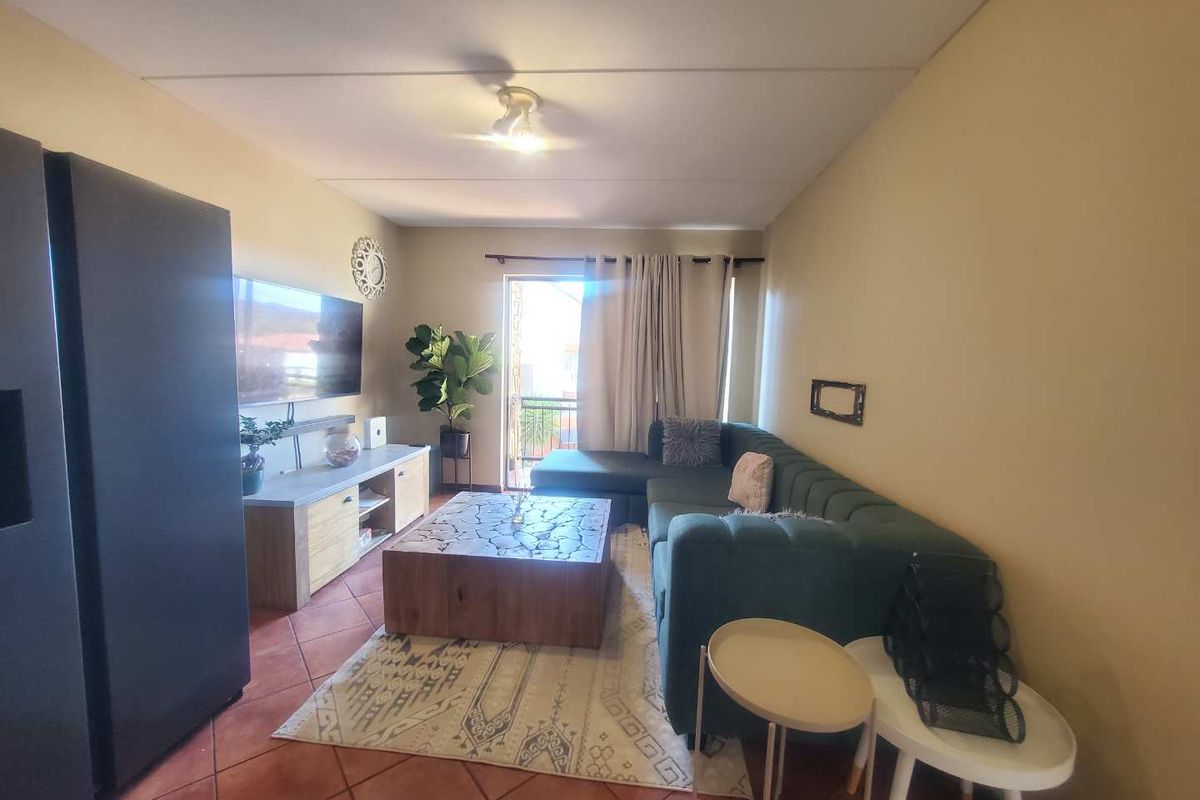 A comfortable living room featuring terracotta floor tiles and a sliding glass door leading to a balcony, providing natural light to the space.