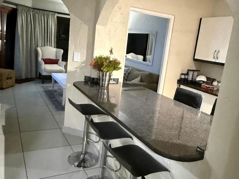 Open plan living area featuring a granite breakfast bar, arched architectural details, and tiled flooring, connecting the kitchen and lounge spaces.