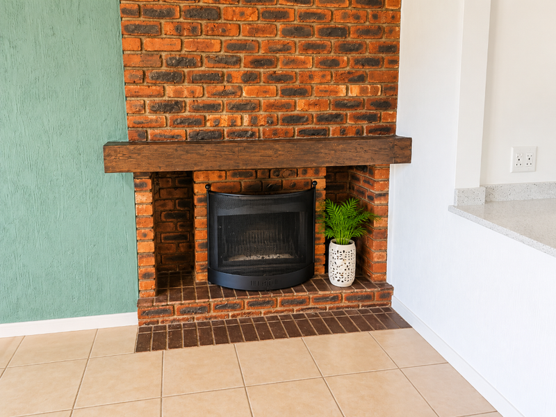 A well-maintained living area featuring a prominent exposed brick fireplace with a timber mantelpiece and neutral ceramic floor tiling.