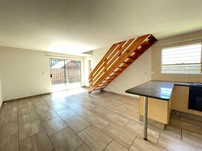 Open-plan living area featuring tiled flooring, a wooden staircase, and a functional kitchen with granite countertops and built-in oven.