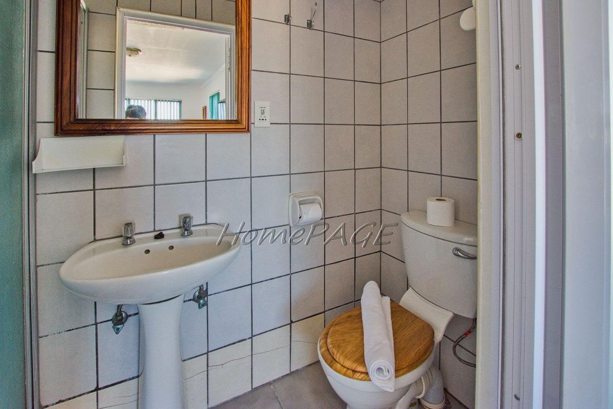 A compact bathroom featuring a pedestal sink, standard toilet, and wall-mounted mirror, finished with white square wall tiles.