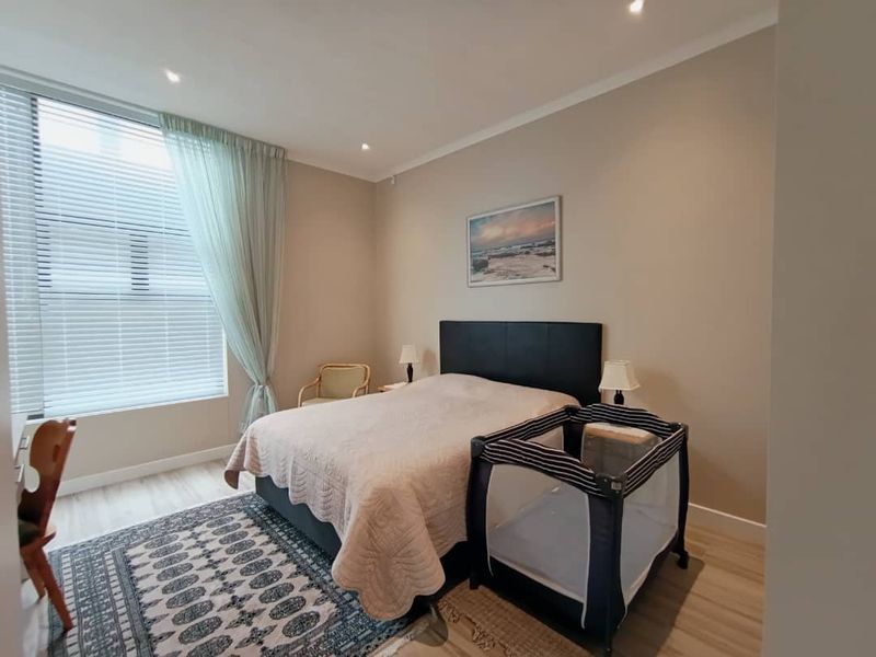 A well-maintained bedroom featuring neutral wall tones, laminate flooring, recessed lighting, and a large window with fitted venetian blinds.