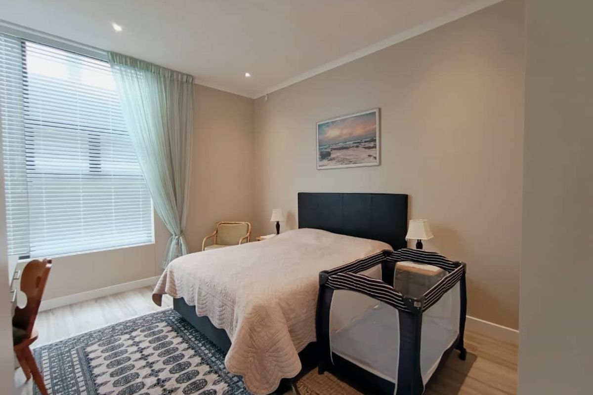 A well-maintained bedroom featuring neutral wall tones, laminate flooring, recessed lighting, and a large window with fitted venetian blinds.