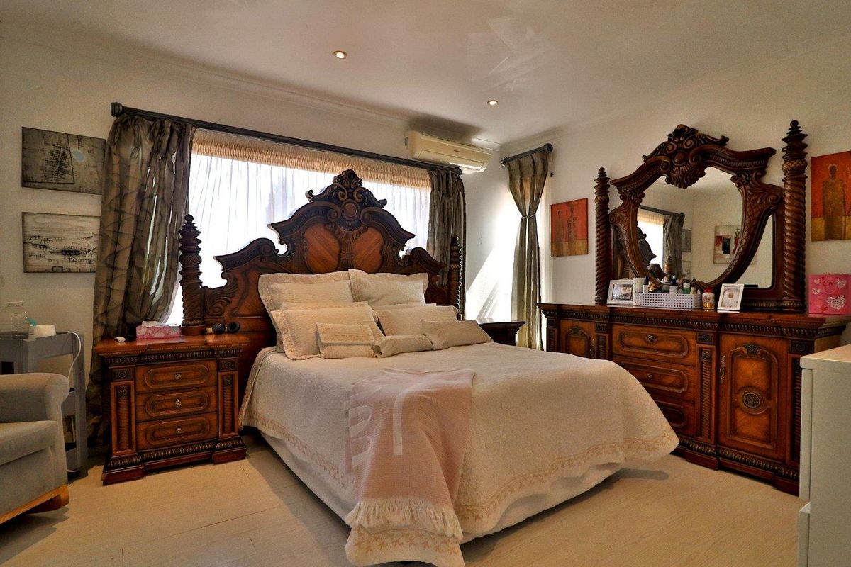 A well-maintained bedroom featuring recessed downlighting, a wall-mounted air conditioning unit, and large windows with curtain tracks.