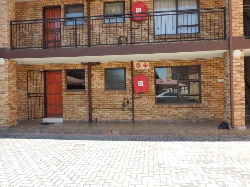 Exterior view of a face brick townhouse complex featuring a paved driveway, ground floor patio, and upper-level balcony with security gates.