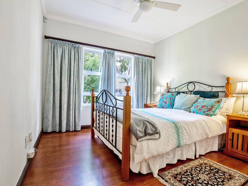 A well-lit bedroom featuring laminate flooring, a ceiling fan, and large casement windows that provide natural light.