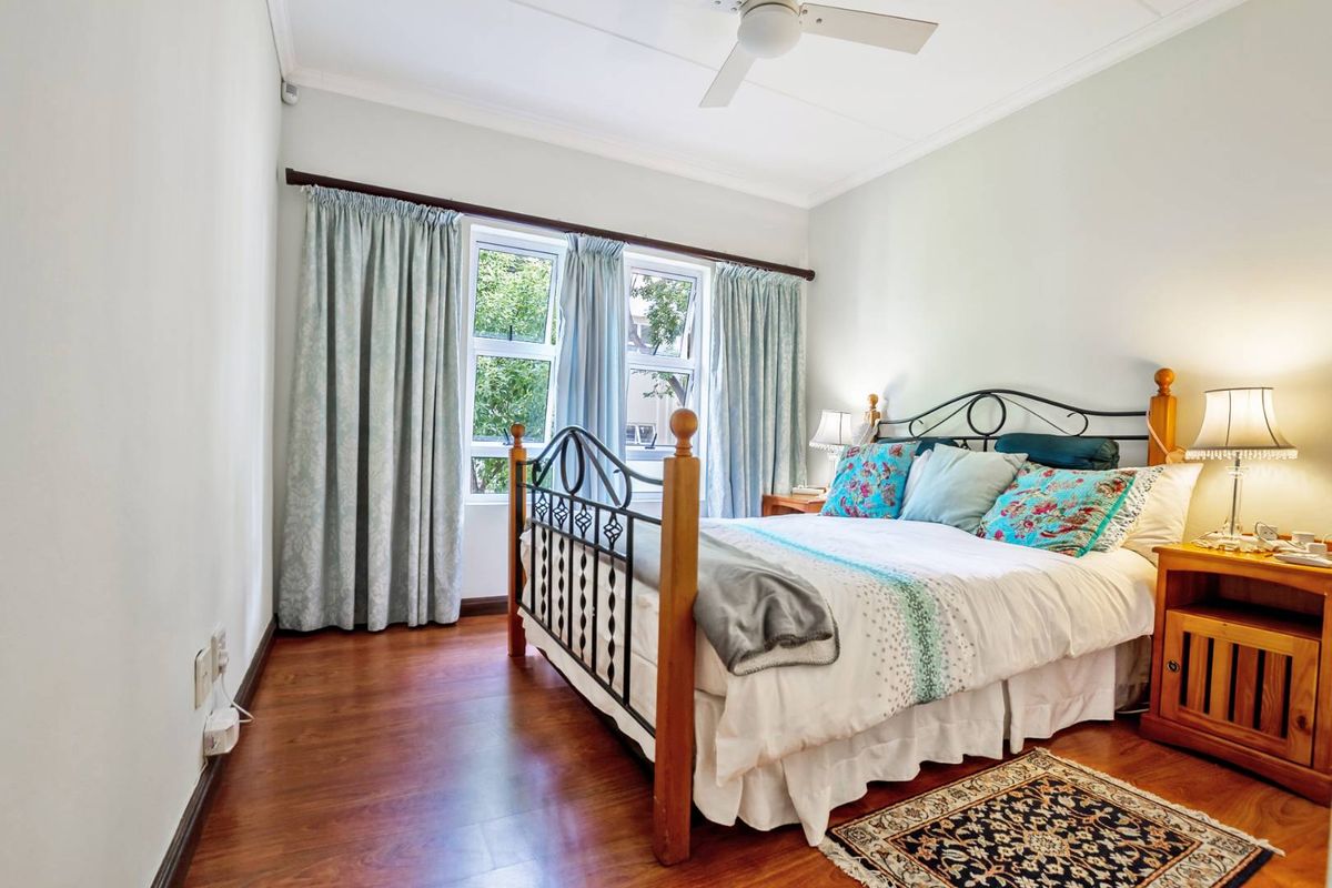 A well-lit bedroom featuring laminate flooring, a ceiling fan, and large casement windows that provide natural light.